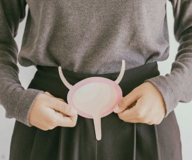 A woman holding a cut out of a bladder over top of her abdomen.