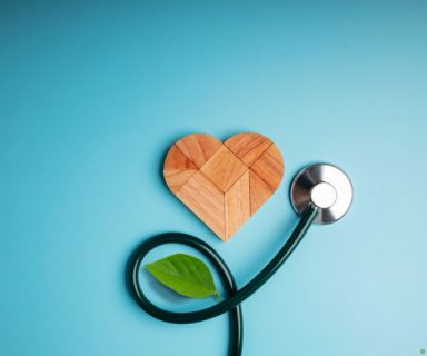 A wooden heart, stethoscope, and small green leaf on a blue background.