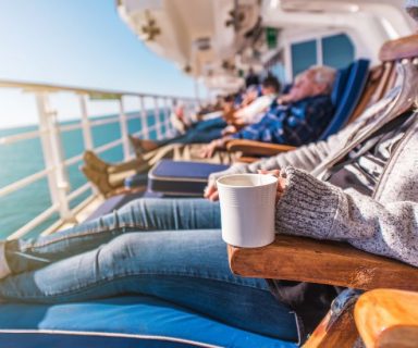 People sitting on lounge chairs on a cruise ship, drinking coffee.