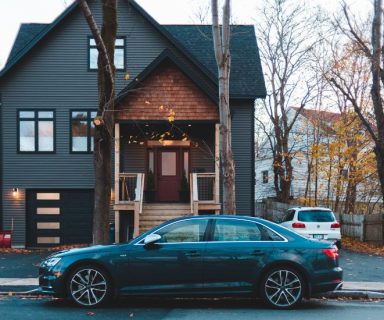 A black sedan car parked in front of a house.